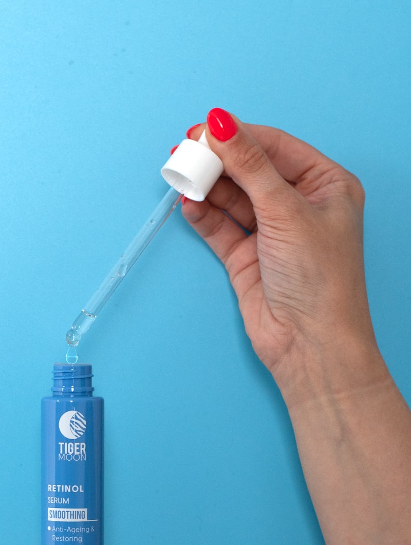 Woman showcasing retinol serum application with a dropper against her vibrant red nails